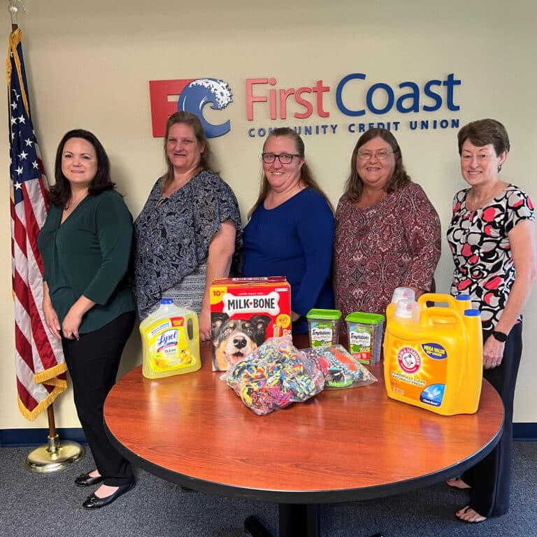 Group of four women standing together beside table with dog treats and toys, cat treats, and dish detergent