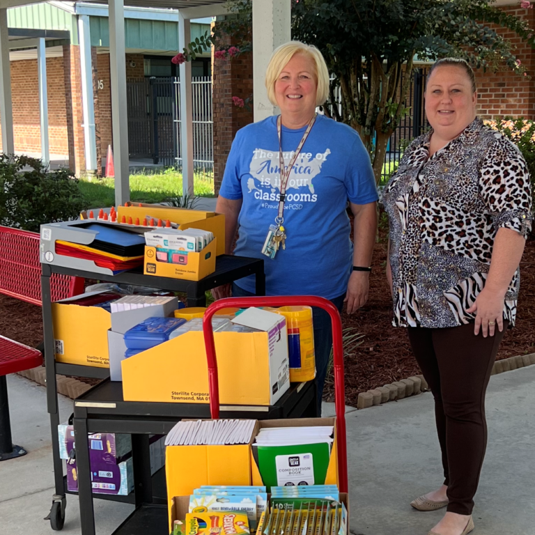 2 women standing outside school with 2 carts full of school supplies