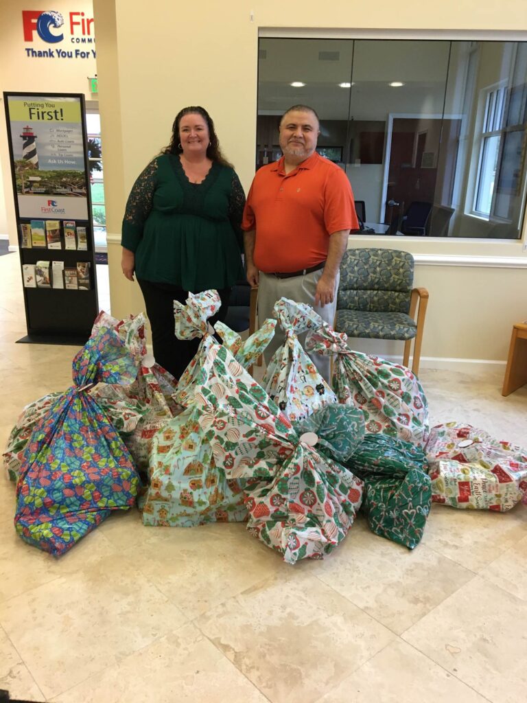 Man and Woman standing next to bags of Christmas presents