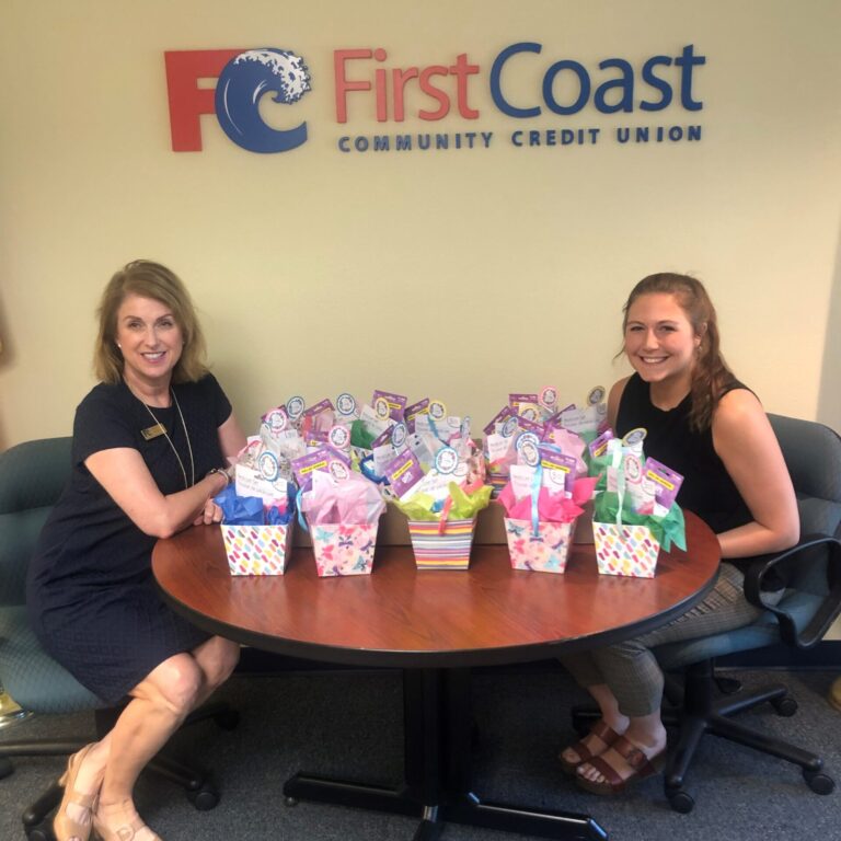 Two women sitting at table with gift baskets between them